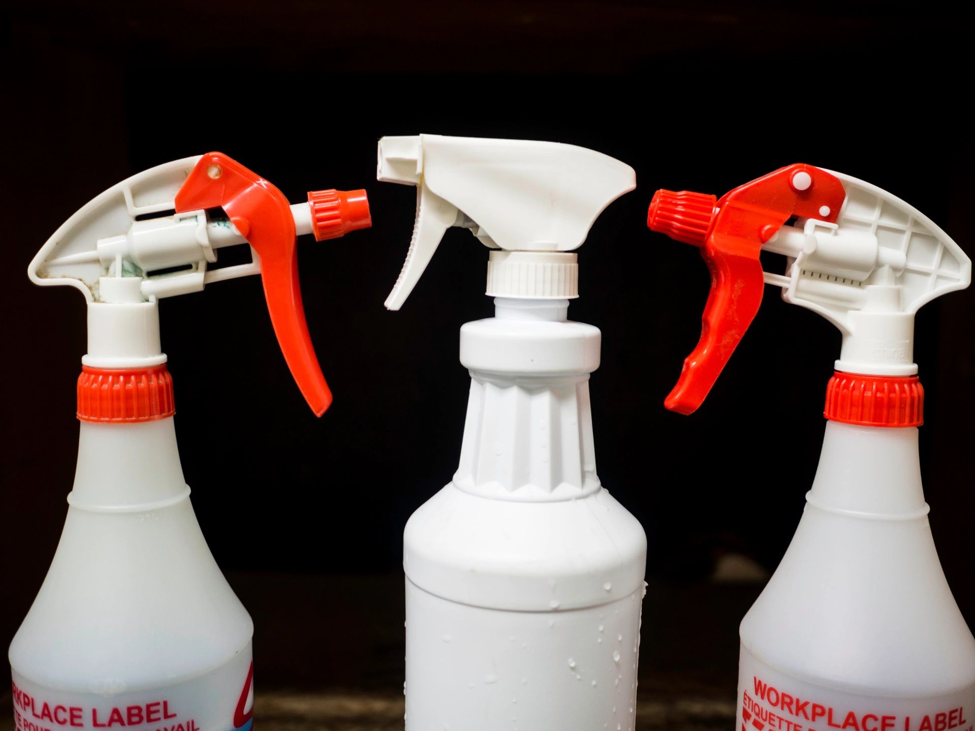 Three cleaning spray bottles - two with read nozzles one with white.