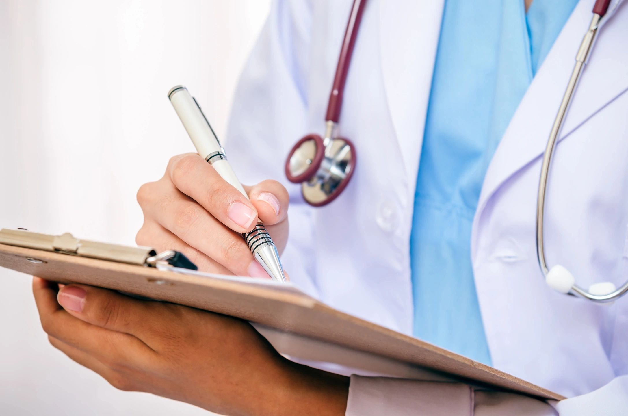 person wearing white coat and stethoscope writing on a clipboard